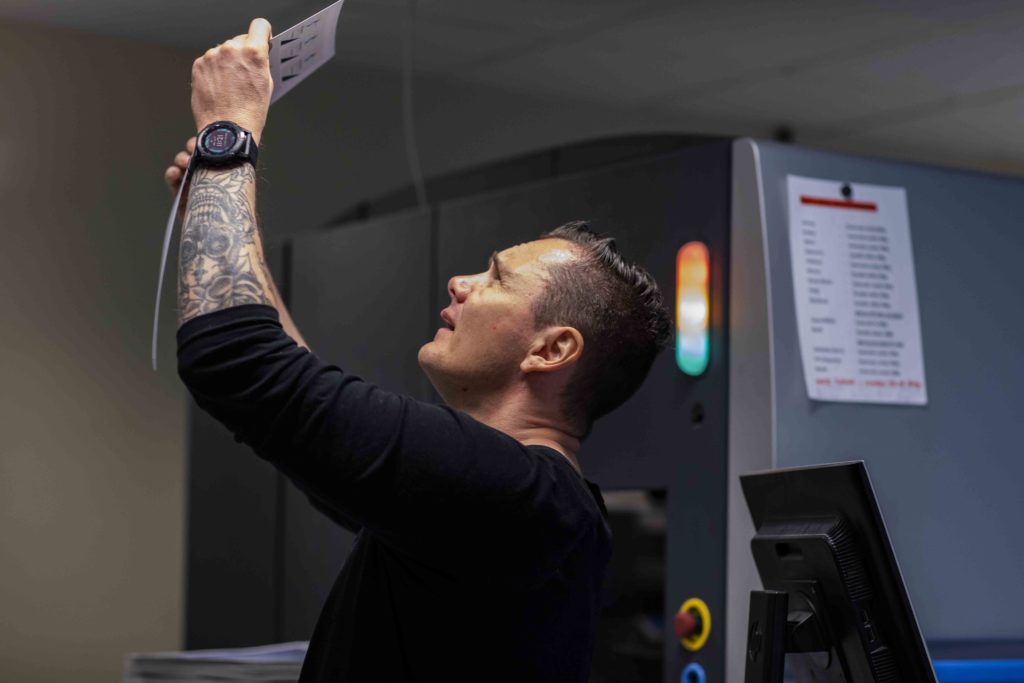 En mann med tatovert arm holder et ark opp mot lyset mens han studerer det.