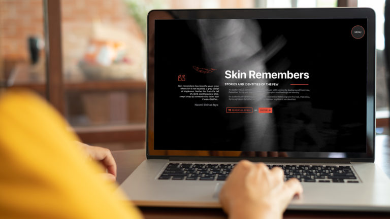 Mockup av kvinne som sitter ved Macbook med nettsiden til Skin remembers,